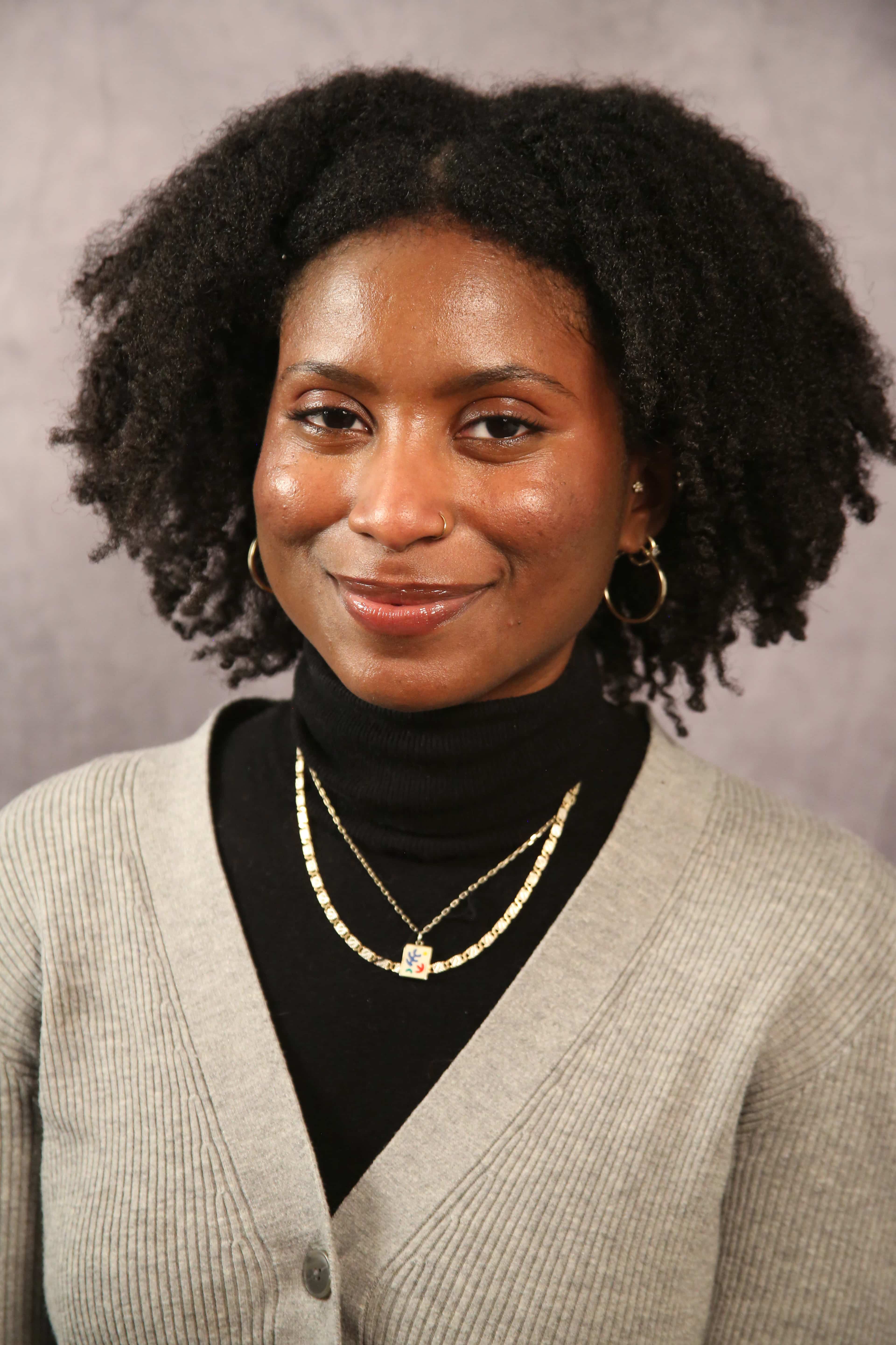 A headshot-style photograph of Abena. Abena has dark skin, black hair, and is smiling.
