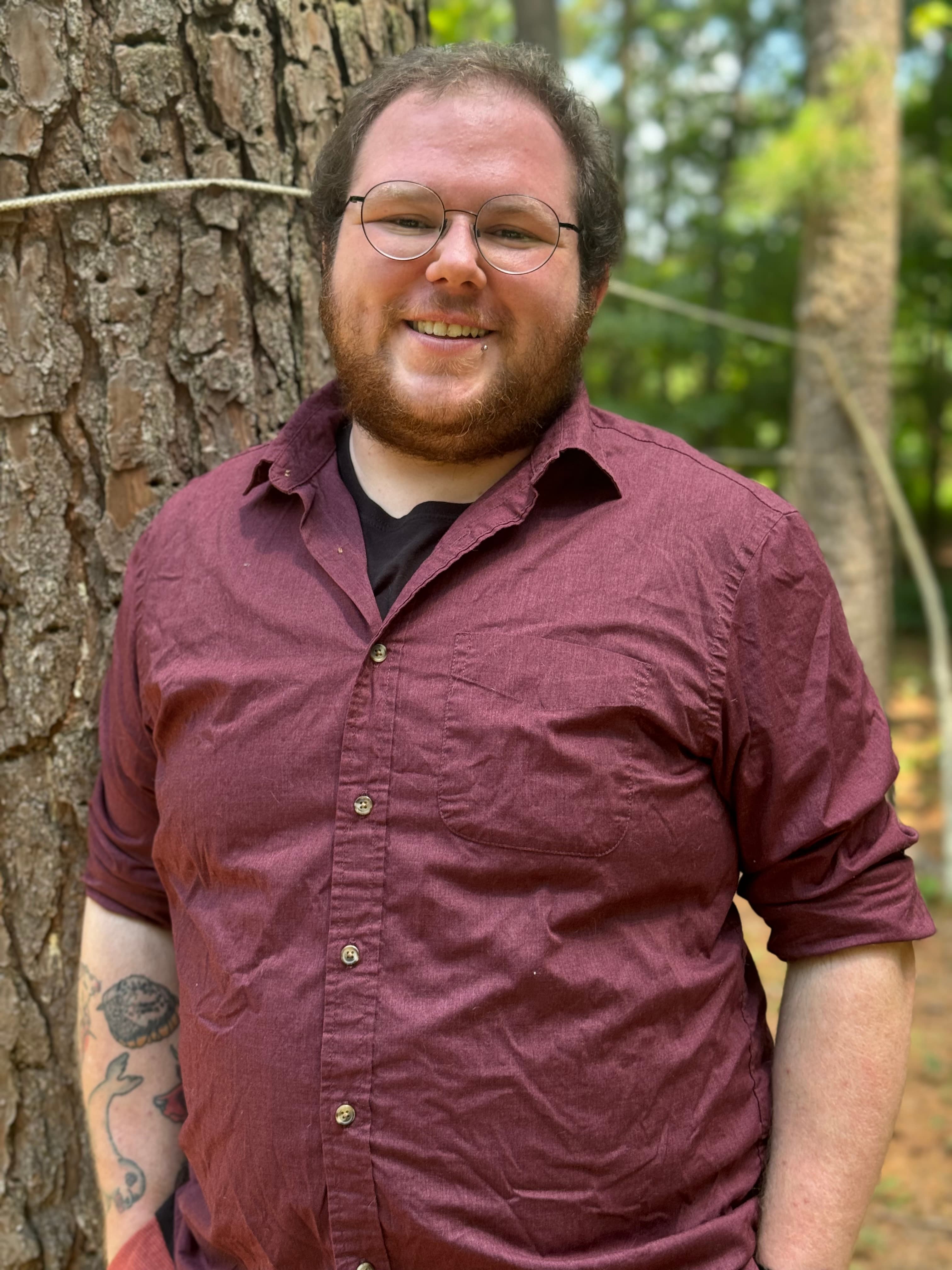 Man with short hair, beard, and red shirt, hands in pockets, looking at the camera