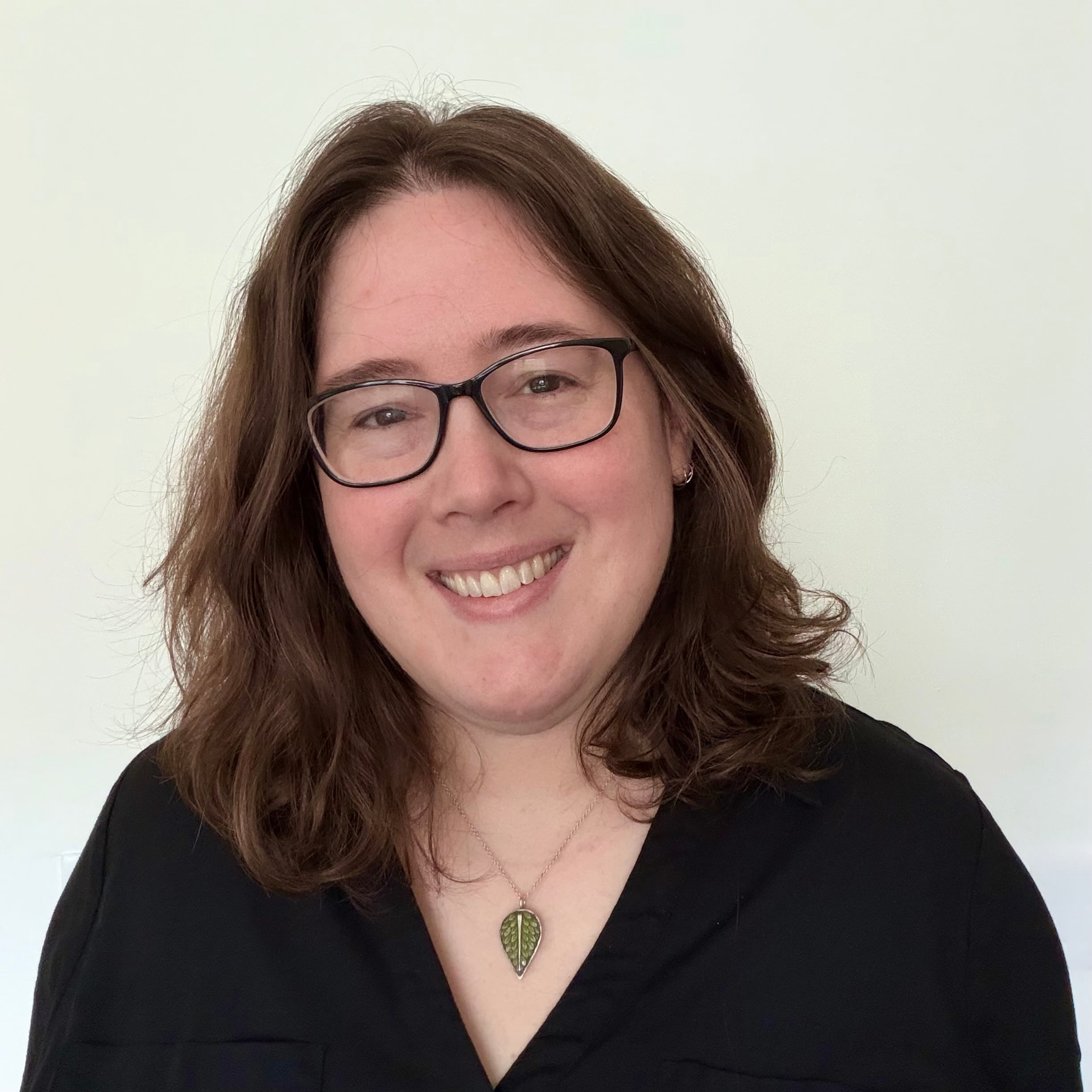 A headshot of Elaine Short, a smiling white woman with shoulder length brown hair and black-rimmed glasses wearing a black button-down.
