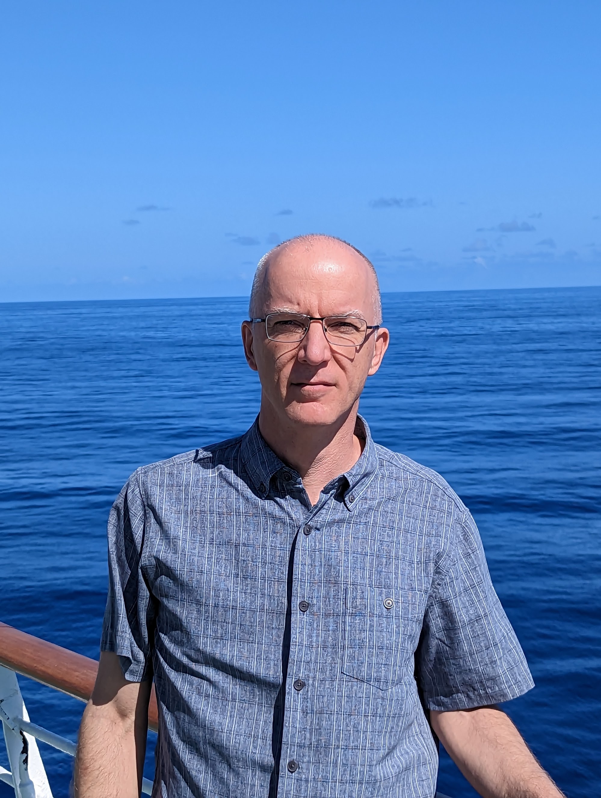 A man with glasses looking at the camera, in front of the ocean