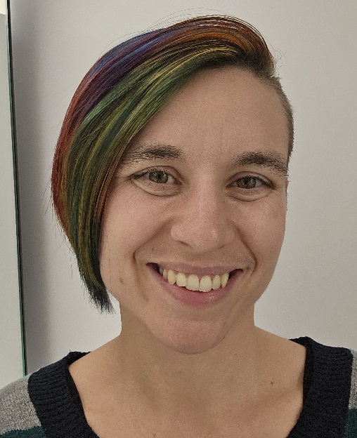 A nonbinary person with rainbow hair and light skin smiling at the camera