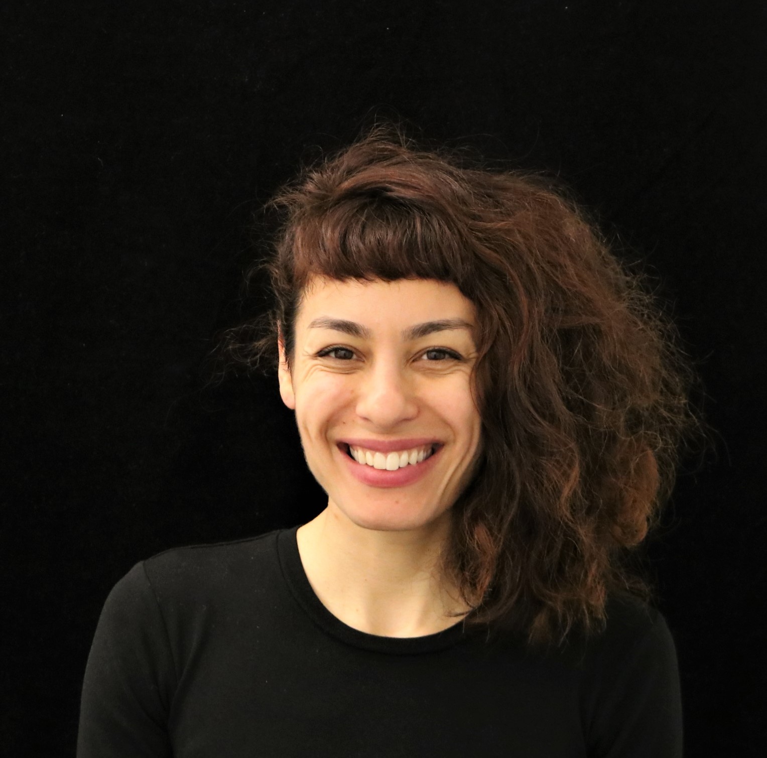 Portrait picture of a Hispanic Caucasian woman with brown wavy hair and brown eyes, smiling.