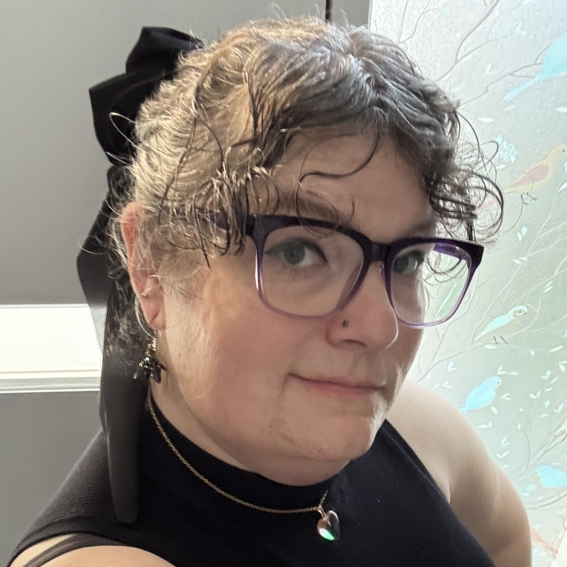 Curly-haired woman with black glasses and hair tie looking at the camera